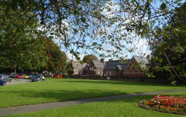 a grassy area in the forefront with a path and houses in the background.