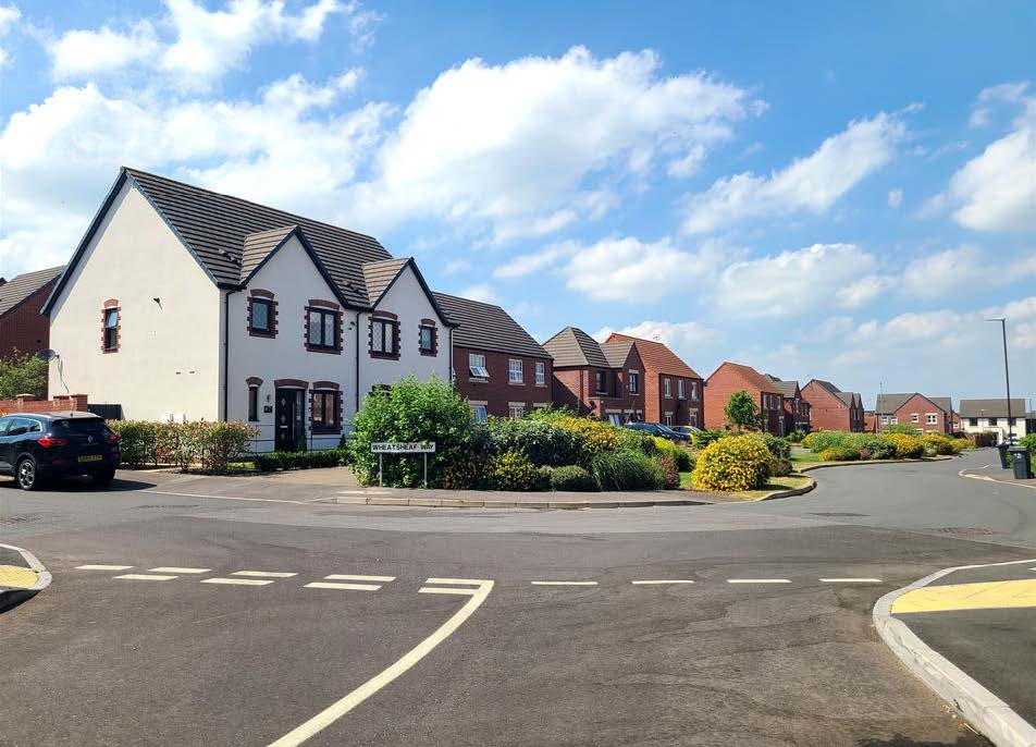 At a street junction with housing in the background overlooking a green area in front.