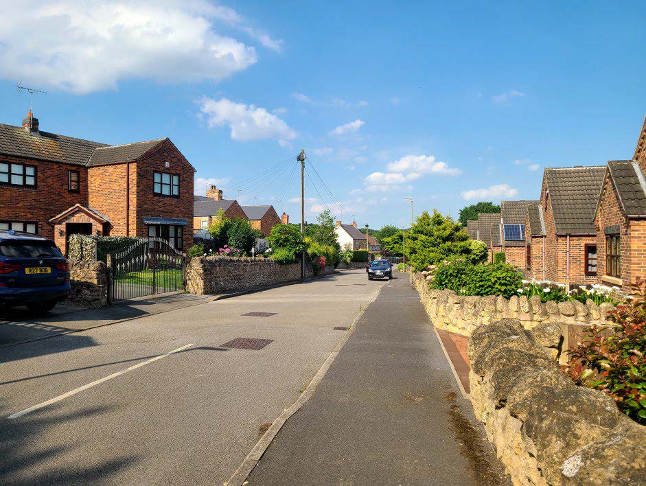 Residential area with houses on either side of the street, with greenery in the front gardens.
