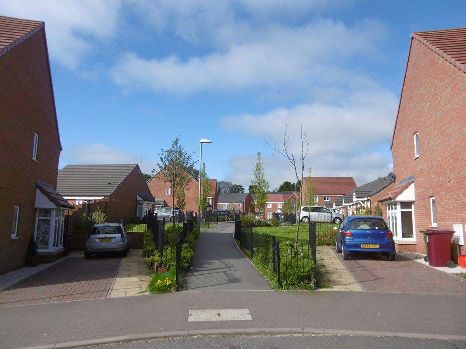 a walking path located within a housing estate with a hose on either side of the path