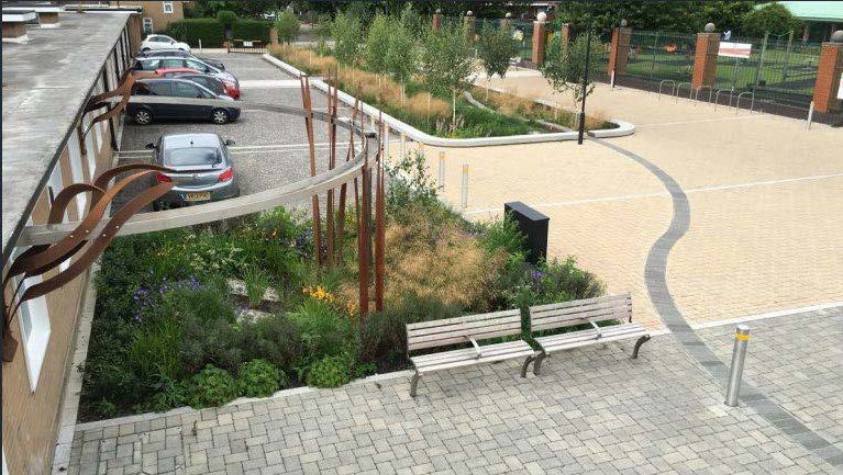 A building on the left with an open space, path and parking on the right.