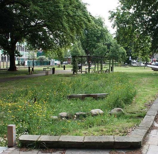 A green area with rocks, wooden structures and benches.