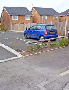 Housing development in the background with a parking area in the foreground, separated by a 6ft fence.