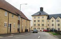 On a road with a large building at the back and houses to the left.
