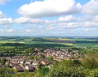 A panoramic view of a small town with rooftops, green fields in the distance, and a partly cloudy sky overhead.